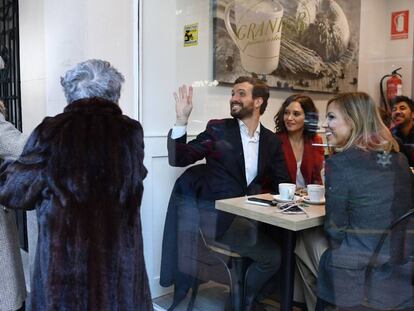 El candidato del PP a las generales, Pablo Casado, sentado junto a la presidenta de la Comunidad de Madrid, Isabel Díaz Ayuso, y su esposa, Isabel Torres, saluda a dos mujeres desde la cafetería donde han desayunado tras votar.
