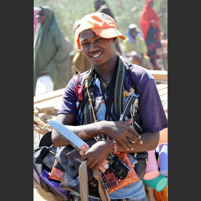 2012, Kenia. Dadaab es el otro gran campo de refugiados de Kenia. Sus primeras secciones se establecieron en 1991 para albergar a refugiados somalíes que huían de la guerra. Como en Kakuma, a lo largo de los años, también ha surgido una intensa actividad económica. Los vendedores ambulantes y los transportistas se suelen congregar alrededor de los puestos de distribución de alimentos para aprovechar el bullicio. El chico de la imagen, después de un rato pululando a nuestro alrededor, consiguió vencer su timidez para pedirme que lo fotografiara con sus productos. La gorra de medio lado formó parte de los preparativos.