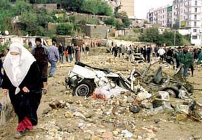 Habitantes de Argel caminan junto a los restos de unos vehículos arrastrados y destrozados por los torrentes causados por el temporal.