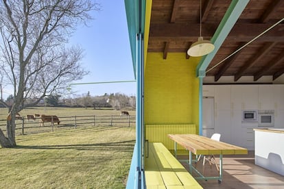 Una distribución abierta hace convivir la cocina —con carpintería blanca y encimera de roble—, el comedor y la sala de estar. Un gran ventanal conecta el interior al paisaje. Luis, un ganadero vecino, cuida del prado de la familia a cambio de que sus vacas puedan comer la hierba fresca.  Cada vez más personas se inclinan por el tránsito permanente entre el campo y la ciudad. Eso fomenta que el habitante rural y el urbano lo sean a tiempo parcial. Ana Sáenz, Manolo García y sus cuatro hijas son rururbanos: su tiempo se confunde entre Cercedilla, a 57 kilómetros de Madrid, y la capital. Ella heredó una casona de fin de semana, levantada sin aislamiento térmico y sin relación con el paisaje. Decidieron acondicionarla progresivamente, y los arquitectos Lys Villalba y Enrique Espinosa cuidaron tanto el confort interior como el consumo energético y la relación con el exterior. Hoy las vacas de su vecino Luis pastan en el prado de su casa vieja y nueva. El revestimiento de cerámica diferencia lo nuevo: una zona de estar, la habitación de las hijas —en la antigua leñera— y un cuarto para la calefacción. Los viejos muros de piedra están cortados y una estructura metálica abre la zona de estar hacia el paisaje. Ya nada está en su sitio. Ahora el viejo techo es mesa: las traviesas que formaban la cubierta se han recuperado para construir el mobiliario y de las contraventanas se han hecho puertas. Así, la casa irá creciendo. Tendrá una segunda vida, como la que ha construido esta familia entre el campo y la ciudad.