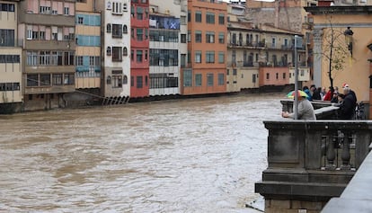 Varias personas contemplan el paso del río Onyar, desbordado por el temporal de lluvias.