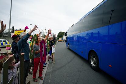 Varios personas saludan a un autocar que transporta a solicitantes de asilo que llegan al buque 'Bibby Stockholm', reconvertido en centro de migrantes, en el puerto de Portland,  este lunes.