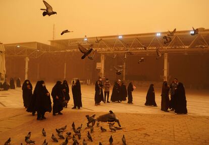 Los visitantes toman fotografías mientras alimentan a las palomas durante una tormenta de arena en la ciudad santa de Najaf en Irak el 16 de mayo de 2022.