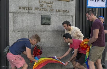 Un grupo de personas con la bandera del arco iris se paran frente a la embajada de Estados Unidos en Madrid.