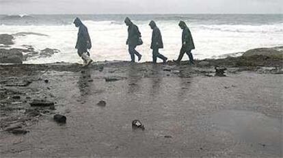 Unos voluntarios examinan la playa de Muxia, completamente cubierta de fuel.