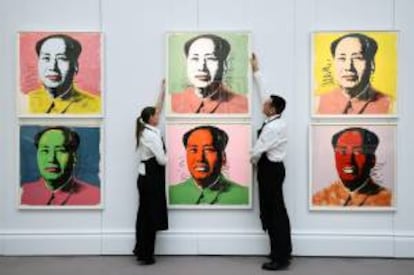 Dos trabajadores colocan varias obras de arte del artista Andy Warhol en las que se retrata al revolucionario comunista chino Mao, en la casa de subastas Sotheby's, Londres, Reino Unido.
