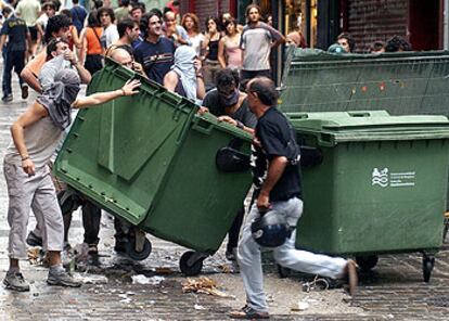 Un grupo de jóvenes cruza un contenedor en la calle durante los disturbios por el desalojo de un centro <i>okupa</i> en Pamplona.