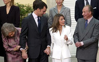 La Reina mira los gemelos de zafiros y oro blanco regalo de Letizia Ortiz al Príncipe en la petición de mano, mientras el Rey habla con la pareja.