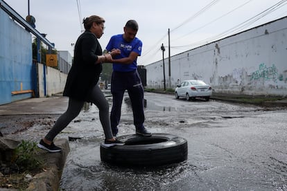 Vecinos de la colonia San Lorenzo, en la alcaldía Iztapalapa, cruzan una calle inundada con el apoyo de un neumático. Este martes en Ciudad de México. 