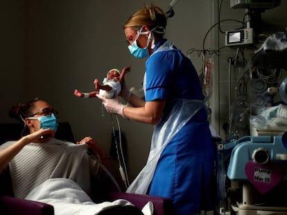 LA VIDA EN MEDIO DEL CAOS. Con guantes y mascarilla, la enfermera Kirsty Hartley acerca a Theo, un bebé nacido prematuramente en plena primera ola de la pandemia de la covid-19, a su madre, Kirsty Anderson, en la unidad de cuidados intensivos neonatales del hospital general de Burnley, al norte de Mánchester, en el Reino Unido. La foto fue tomada el 15 de mayo.