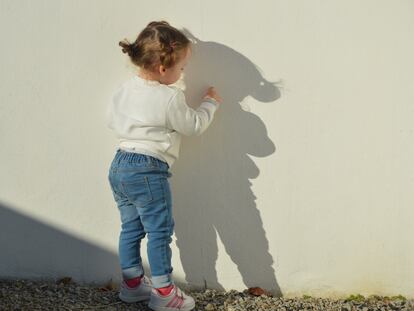 Una niña escribe con su dedo en una pared.