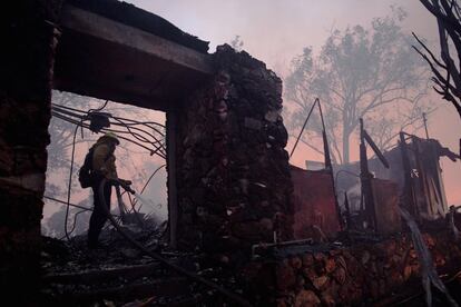 Um bombeiro utiliza a mangueira em uma casa fumegante destruída pelo incêndio em Los Angeles.