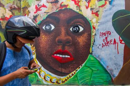 Un chico con un casco escribe en su móvil mientras pasa por delante de uno de los grafittis de la Comuna 13 de Medellín. Estos murales son parte del paisaje urbano del barrio.