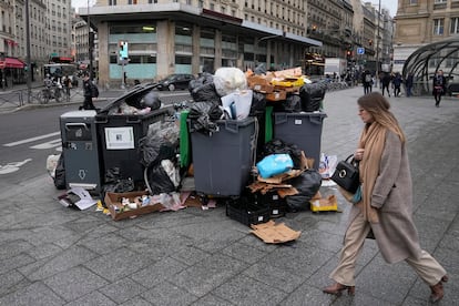 A woman walks past a pile of garbage cans Tuesday, March 7, 2023 in Paris.