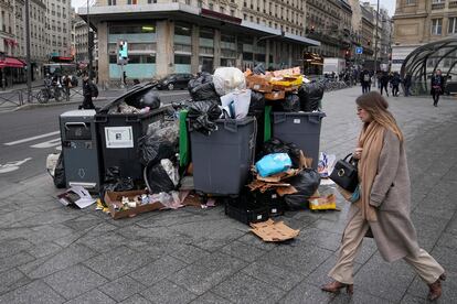 A woman walks past a pile of garbage cans Tuesday, March 7, 2023 in Paris.