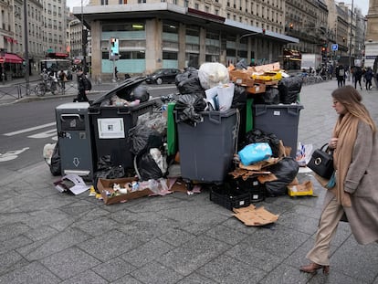 A woman walks past a pile of garbage cans Tuesday, March 7, 2023 in Paris.