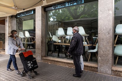 Dos personas pasan delante de un bar cerrado por el confinamiento.