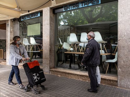 Dos personas pasan delante de un bar cerrado por el confinamiento.