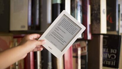 Un libro electrónico ante una librería de volúmenes de papel.