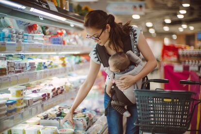 Una joven madre con su bebé compra productos lácteos en un supermercado.