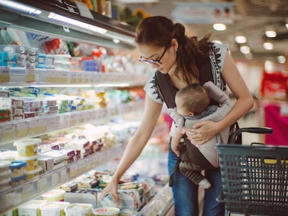 Una joven madre con su bebé compra productos lácteos en un supermercado.