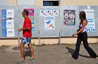 Dos votantes pasan junto a carteles que piden el voto para el <i>sí</i> y el <i>no</i> en Ajaccio.