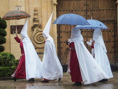 Unos nazarenos de la Hermandad de La Sentencia se protegen de la lluvia este lunes en Sevilla.