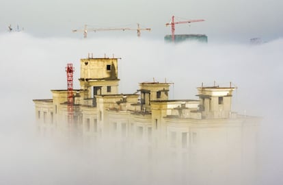 Grúas y edificios residenciales en construcción asoman sobre una espesa niebla en Anyang (China).