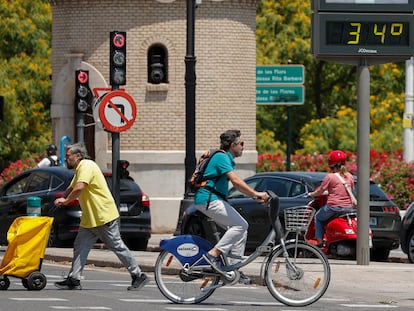 Varias personas pasan junto a un termómetro que marca 34 grados en una calle de Valencia, este lunes.