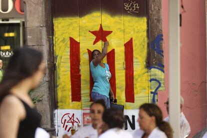 En la imagen una mujer en alto junto a una pintada de una estelada. A unos días de la fecha del referéndum y a pesar de los golpes logísticos sufridos, el Govern insiste en que habrá votación y que, en el caso de ganar el sí, dos días después el Parlament proclamará la independencia.