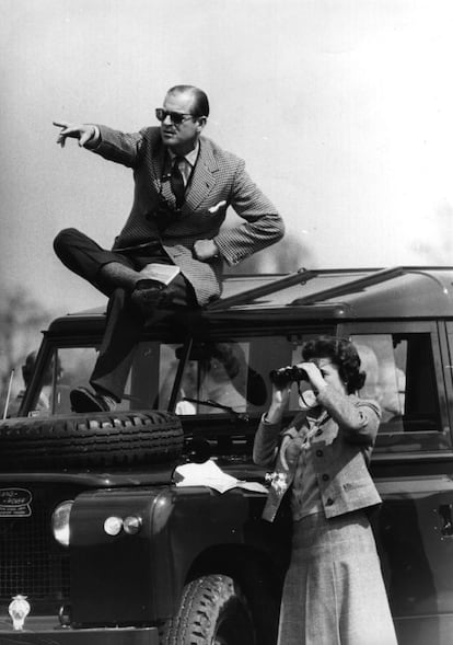 O duque de Edimburgo, sentado no teto de um Land Rover, sinaliza para os participantes da competição de saltos com cavalos em Badminton, enquanto a rainha Elizabeth II observa pelos binóculos, em 20 de abril de 1968.