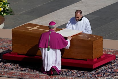 Archbishop Diego Giovanni Ravelli, with his back turned, kneels before the coffin of Pope Francis as he opens the Gospels.