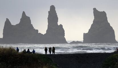 Varias personas pasean en un playa de arena negra, cerca del volcán Katla, en Islandia. 