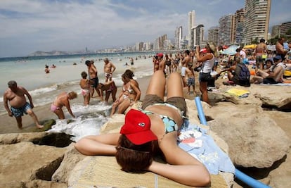 Una turista toma el sol sobre las rocas en una playa en Benidorm.