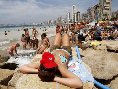 Una turista toma el sol sobre las rocas en una playa en Benidorm.