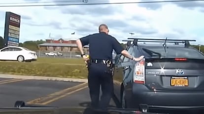A police officer touches the back of a car after pulling it over on the highway.