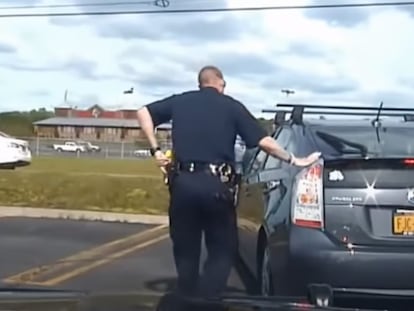 A police officer touches the back of a car after pulling it over on the highway.