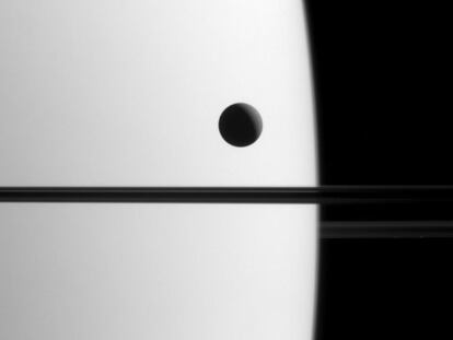 La sonda internacional Cassini captó en esta imagen una de las lunas más grandes de Saturno, Dione, mientras se desplazaba delante del planeta, un fenómeno conocido como tránsito. La línea oscura que atraviesa la imagen por la mitad representa los anillos de Saturno, que no están iluminados desde esta perspectiva, tomada alrededor de un 0,3º por debajo de su plano. La sonda captó esta imagen cuando estaba situada a 2,3 millones de kilómetros de Saturno, el 21 de mayo de este año. La fotografía tiene una escala de 14 kilómetros por píxel.