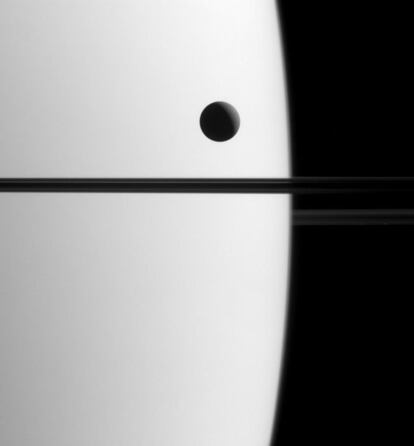 La sonda internacional Cassini captó en esta imagen una de las lunas más grandes de Saturno, Dione, mientras se desplazaba delante del planeta, un fenómeno conocido como tránsito. La línea oscura que atraviesa la imagen por la mitad representa los anillos de Saturno, que no están iluminados desde esta perspectiva, tomada alrededor de un 0,3º por debajo de su plano. La sonda captó esta imagen cuando estaba situada a 2,3 millones de kilómetros de Saturno, el 21 de mayo de este año. La fotografía tiene una escala de 14 kilómetros por píxel.