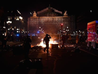 Un policía y un bombero, ante un contenedor de basura en llamas ante el edificio de la ópera de de París, durante una manifestación este 20 de marzo.