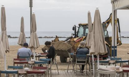 Una retroexcavadora reposa sorra en una platja de la Barceloneta.