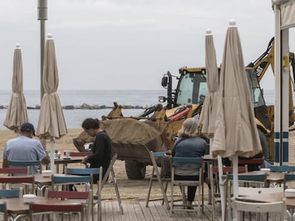 Una retroexcavadora reposa sorra en una platja de la Barceloneta.