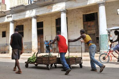 Dos hombres empujan carretillas con cajas de fruta y verdura para vender en La Habana.