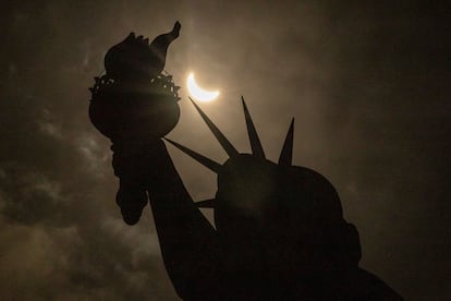 La luna cubre parcialmente el sol detrás de la Estatua de la Libertad durante el eclipse solar total en Nueva York.