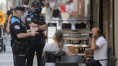 Dos agentes de la policía local de A Coruña se dirigen a un hombre que fuma en una terraza de un bar.