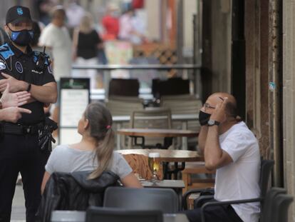 Dos agentes de la policía local de A Coruña se dirigen a un hombre que fuma en una terraza de un bar.