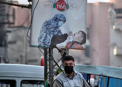 Un hombre con mascarilla junto a un cartel que promueve una campaña de polio en un mercado en Peshawar, Pakistán, el 14 de diciembre de 2020.