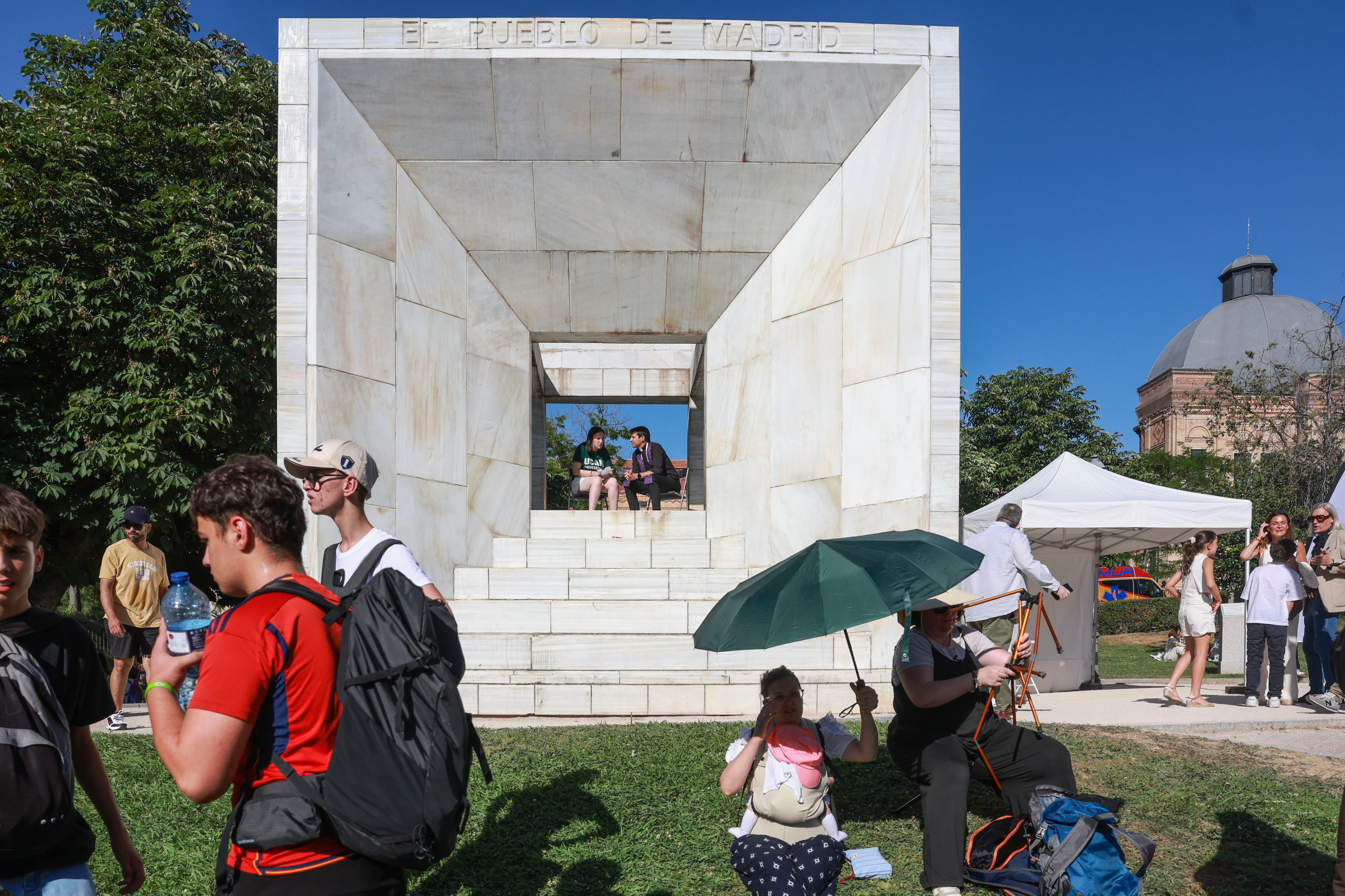 Un cura oía en confesión a una joven, en el monumento a la Constitución, en la plaza de San Juan de la Cruz.