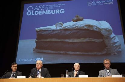 Oldenburg (segundo por la derecha), junto al director general del Guggenheim, Juan Ignacio Vidarte (a su derecha); Achim Hochdörfer, comisario de la exposición, y Rafael Pardo, director de la Fundación BBVA (primero por la izquierda), en la presentación de la muestra Detrás, el cartel de la misma, con una imagen de la obra 'Tarta en el suelo'.