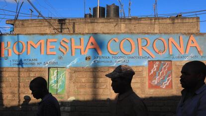 Tres hombres pasan frente a una pintada en la que se lee 'Para al corona' en suajili, en Mathare, un barrio marginal de Nairobi (Kenia).